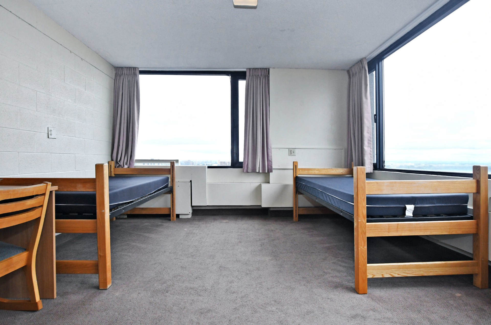 Photo d'une chambre double dans la résidence Stong. Deux lits et deux fenêtres au milieu de la chambre.