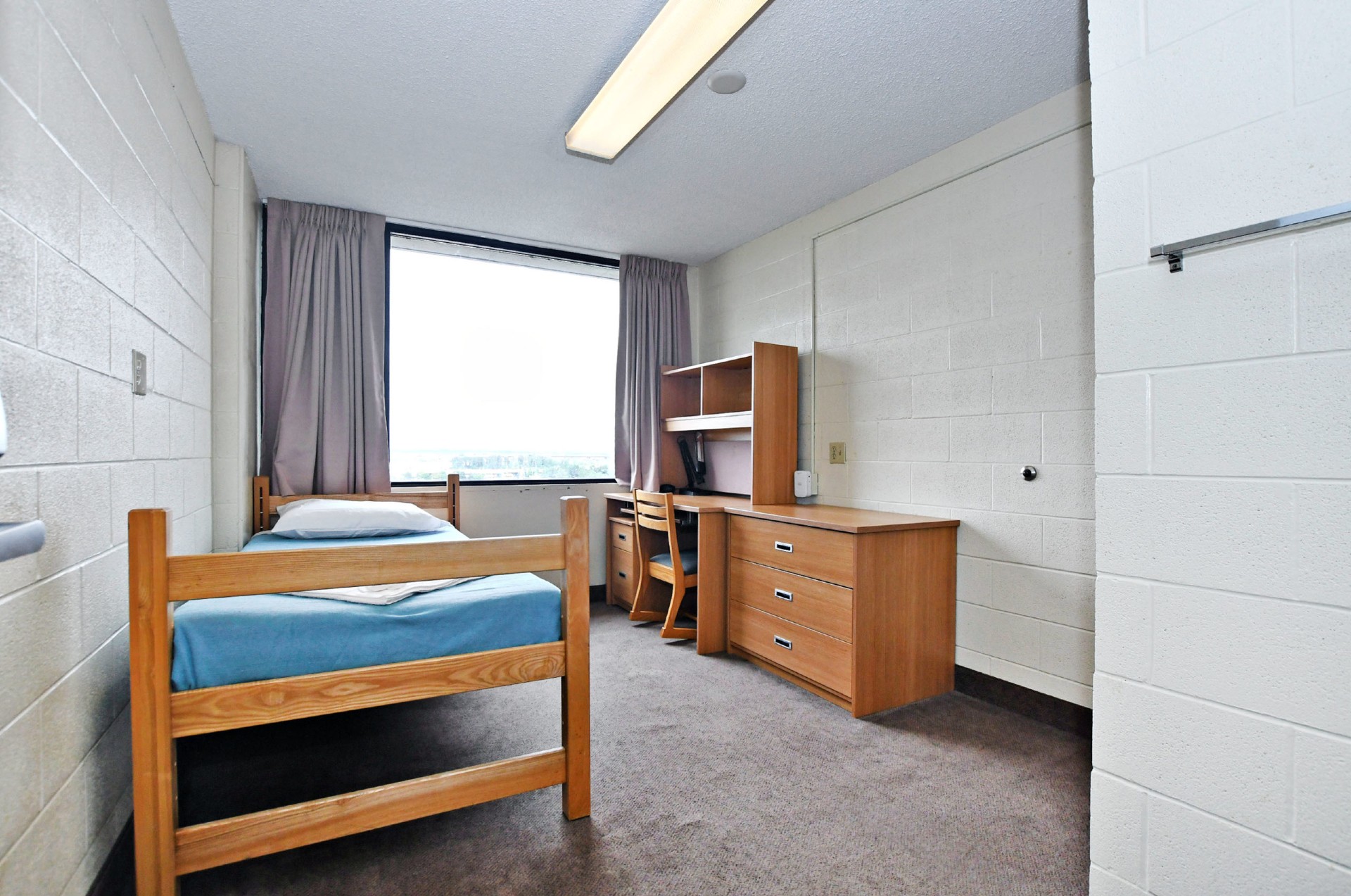 Picture of the single room in Bethune building, a bed and a desk with a window in the middle of the room