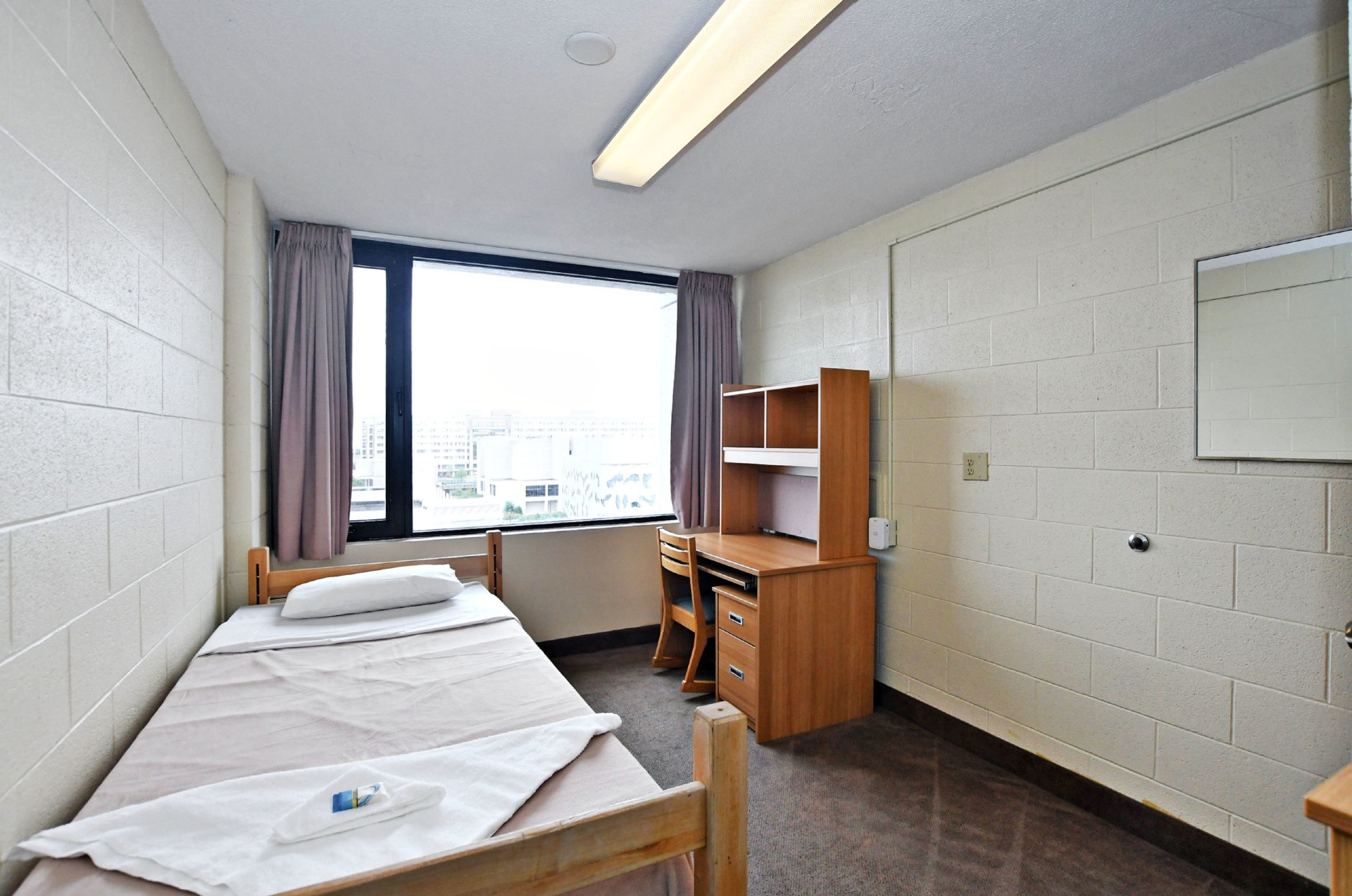 Picture of the single room in Stong building, a bed and a desk with a window in the middle of the room