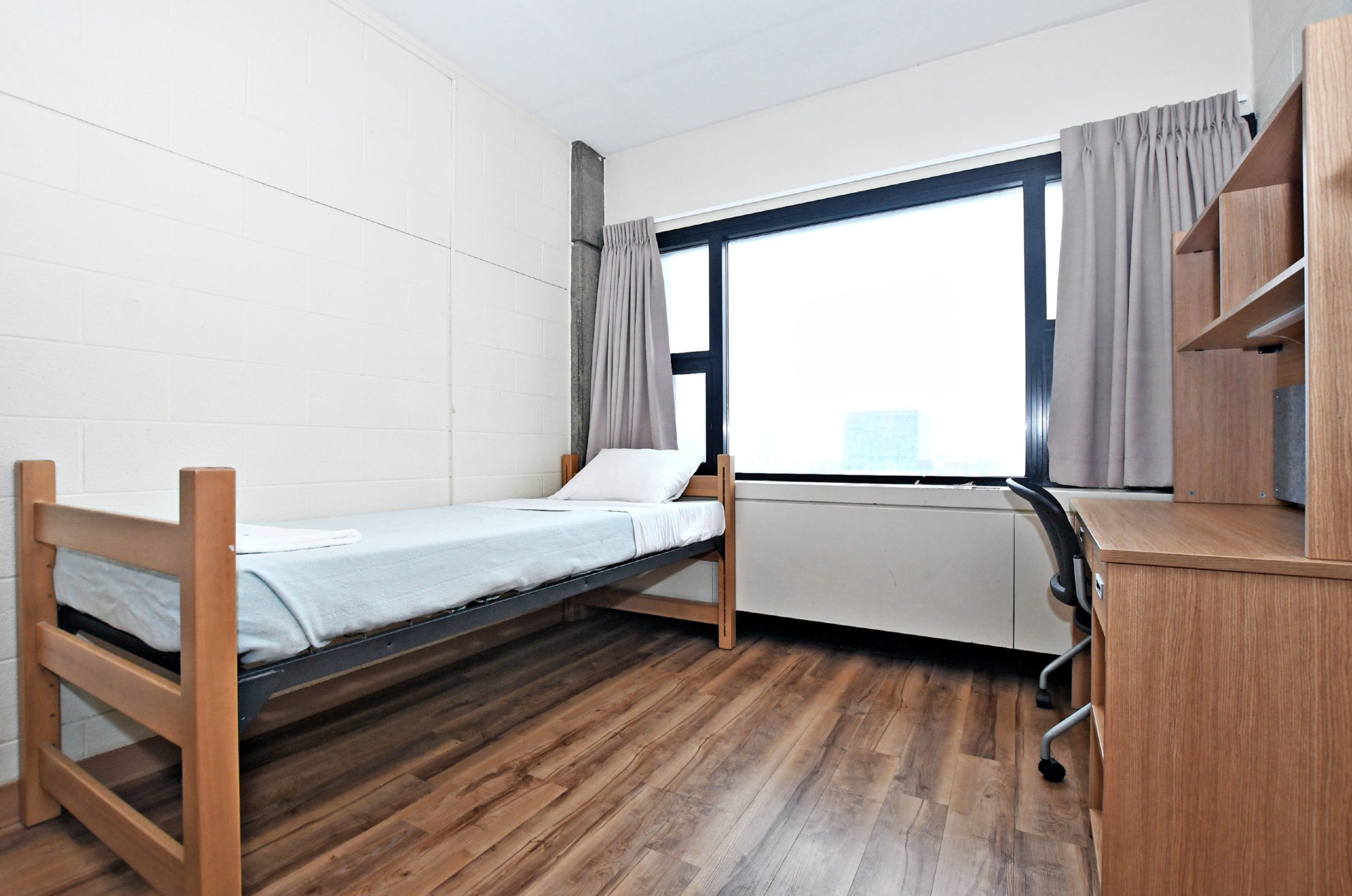 Picture of the single room in Tatham-Hall building, a bed and a desk with a window in the middle of the room