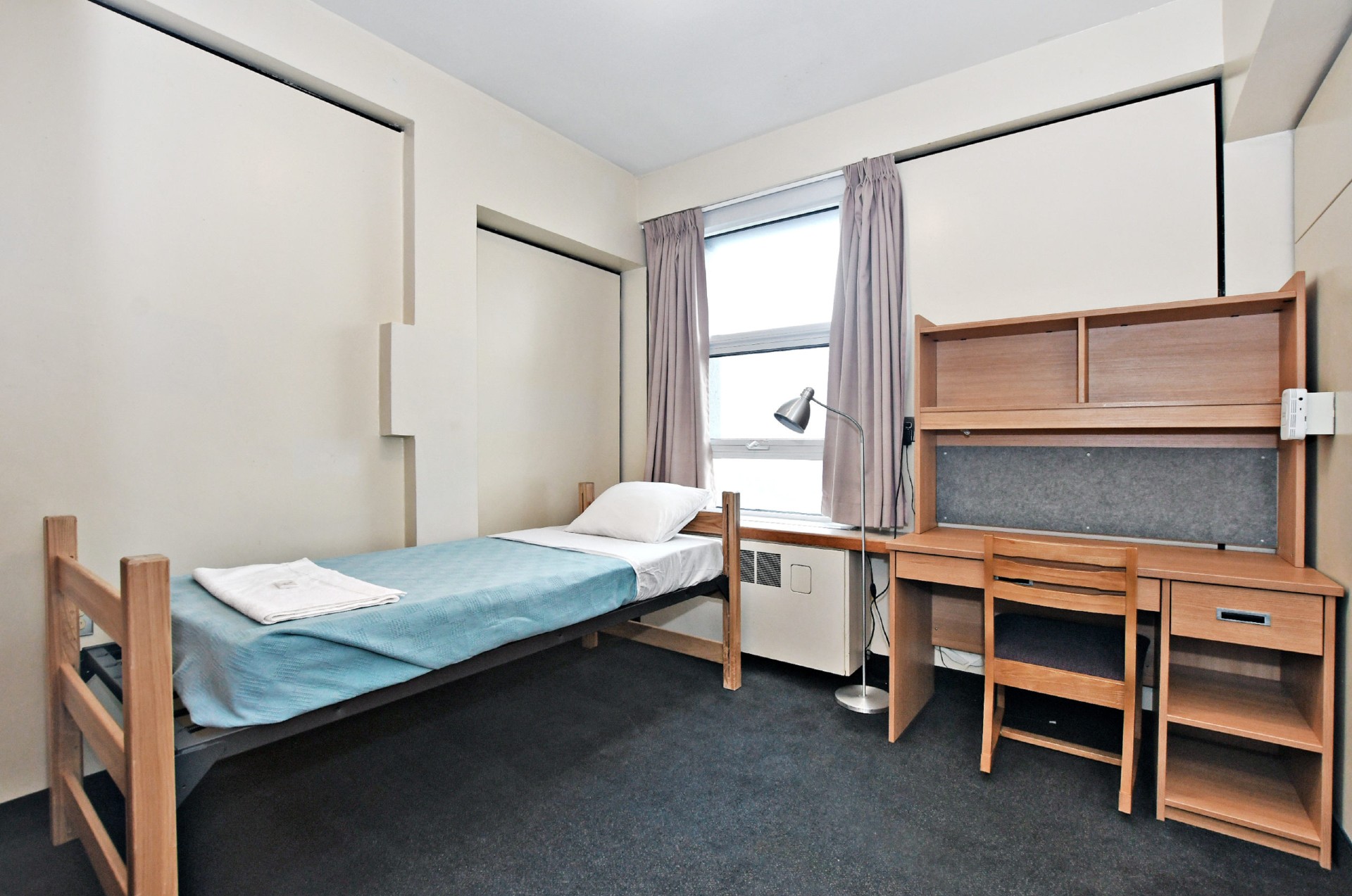 Picture of the single room in Vanier building, a bed and a desk with a window in the middle of the room